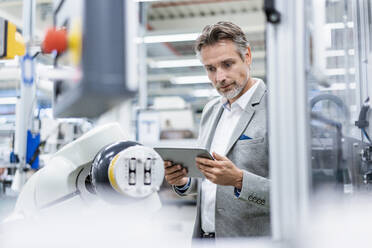 Businessman with tablet at assembly robot in a factory - DIGF07805