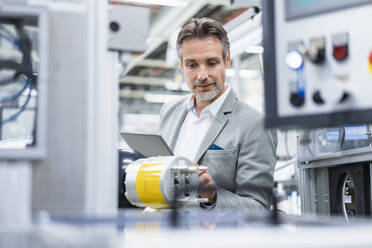 Businessman with tablet at assembly robot in a factory - DIGF07806