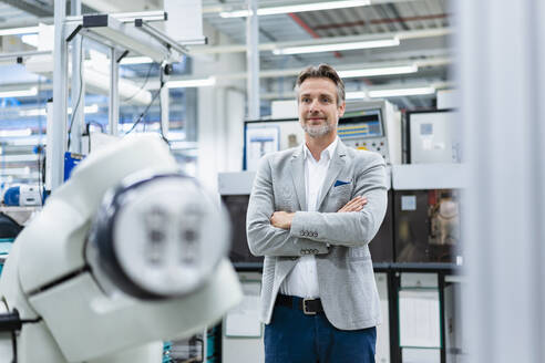 Portrait of confident businessman at assembly robot in a factory - DIGF07815