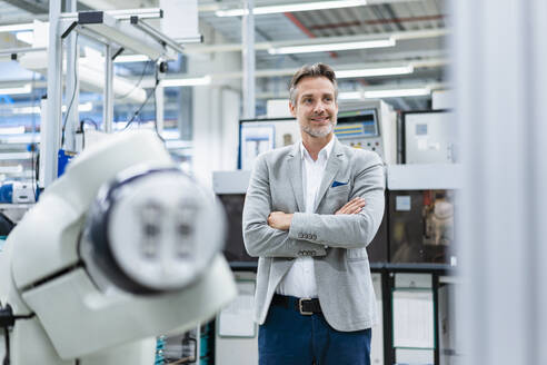 Portrait of confident businessman at assembly robot in a factory - DIGF07816