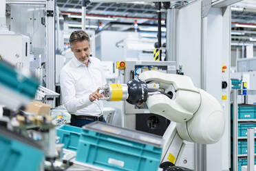 Businessman examining assembly robot in a factory - DIGF07817