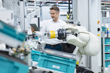 Businessman with tablet at assembly robot in a factory - DIGF07818
