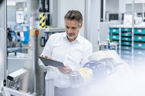 Businessman with tablet at assembly robot in a factory - DIGF07819