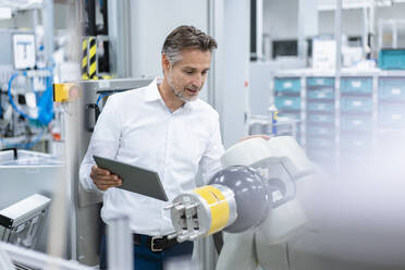 Businessman with tablet at assembly robot in a factory - DIGF07820