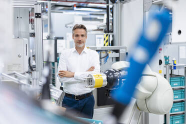Portrait of confident businessman at assembly robot in a factory - DIGF07822
