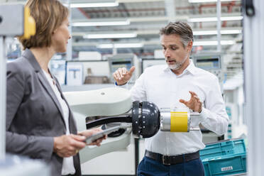 Geschäftsfrau und Mann im Gespräch mit einem Montageroboter in einer Fabrik - DIGF07824