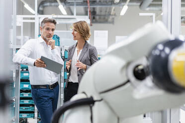 Businesswoman and man with tablet talking at assembly robot in a factory - DIGF07834