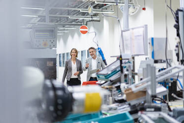 Smiling businesswoman and businessman with tablet talking in a modern factory - DIGF07836