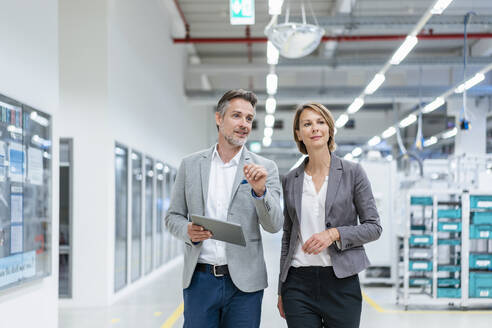 Businesswoman and businessman with tablet walking and talking in a modern factory - DIGF07843