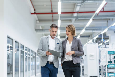 Geschäftsfrau und Geschäftsmann mit Tablet gehen und sprechen in einer modernen Fabrik, lizenzfreies Stockfoto