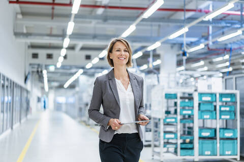 Lächelnde Geschäftsfrau mit Tablet in einer modernen Fabrik, lizenzfreies Stockfoto