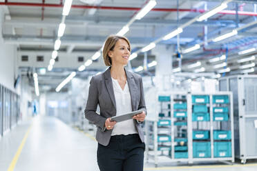 Smiling businesswoman with tablet in a modern factory - DIGF07853