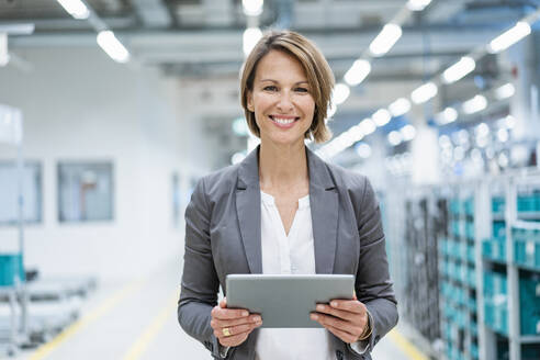 Portrait of smiling businesswoman with tablet in a modern factory - DIGF07868