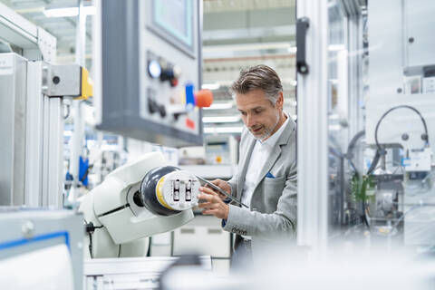 Geschäftsmann mit Tablet am Montageroboter in einer Fabrik, lizenzfreies Stockfoto
