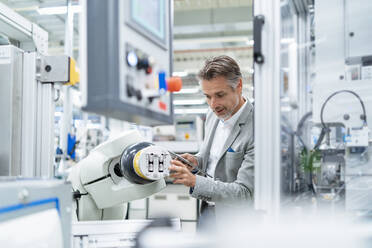 Businessman with tablet at assembly robot in a factory - DIGF07878