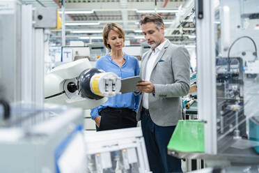 Businessman with tablet and woman talking at assembly robot in a factory - DIGF07880