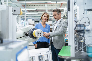 Businessman with tablet and woman talking at assembly robot in a factory - DIGF07881