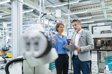 Businessman with tablet and woman talking at assembly robot in a factory - DIGF07883