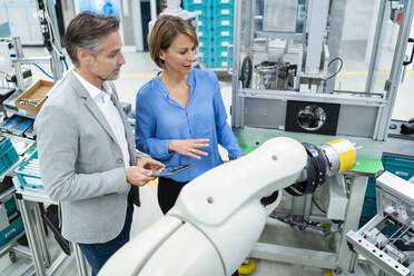 Businessman with tablet and woman talking at assembly robot in a factory - DIGF07885