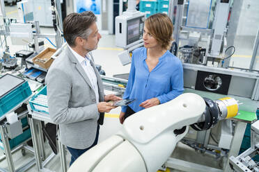 Businessman with tablet and woman talking at assembly robot in a factory - DIGF07886