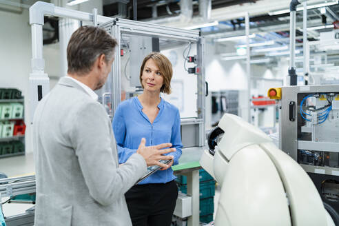 Businessman with tablet and woman talking at assembly robot in a factory - DIGF07887