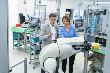 Geschäftsmann mit Tablet und Frau im Gespräch mit Montageroboter in einer Fabrik - DIGF07888