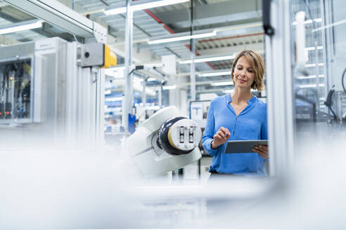Geschäftsfrau mit Tablet am Montageroboter in einer Fabrik - DIGF07891