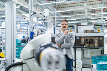 Portrait of confident businessman at assembly robot in a factory - DIGF07892