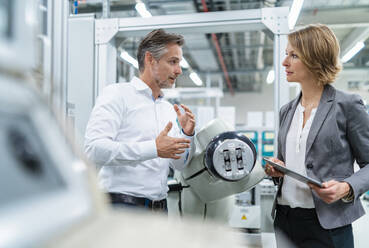 Businesswoman and man talking at assembly robot in a factory - DIGF07894