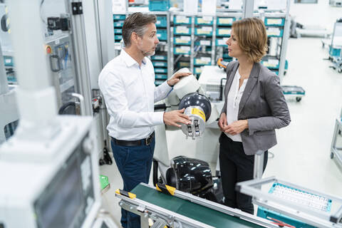 Geschäftsfrau und Mann im Gespräch mit einem Montageroboter in einer Fabrik, lizenzfreies Stockfoto