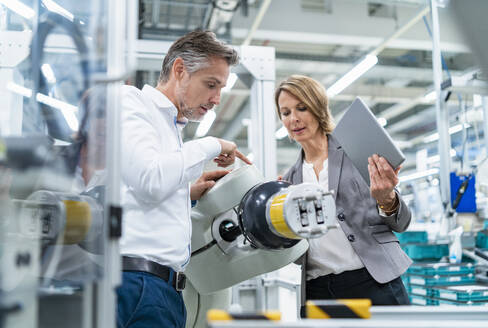 Geschäftsfrau und Mann im Gespräch mit einem Montageroboter in einer Fabrik - DIGF07898