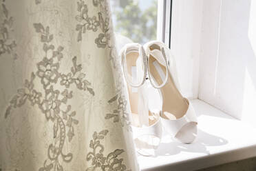 Close-up of wedding sandals by dress on window sill at home - DAWF00901