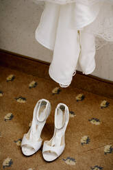 Hohe Winkel Ansicht der Sandalen auf gefliestem Boden unter Hochzeitskleid zu Hause - DAWF00902