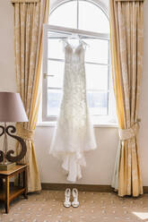 Hochzeitskleid, das zu Hause vor dem Fenster über den Sandalen hängt - DAWF00944