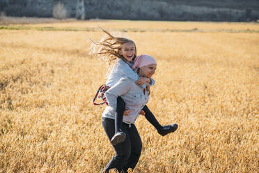 A woman with cancer carrying her daughter on her back, laughing - JCMF00093