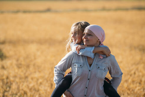 A woman with cancer carrying her daughter on her back, looking sideways - JCMF00094