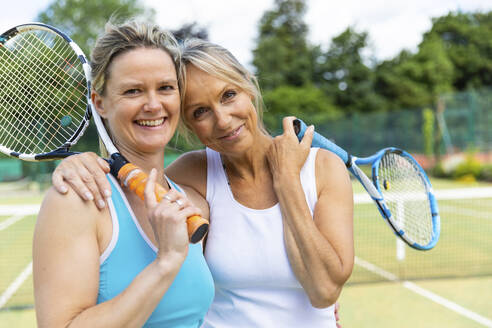 Porträt von zwei glücklichen reifen Frauen auf einem Rasenplatz in einem Tennisclub - WPEF01762