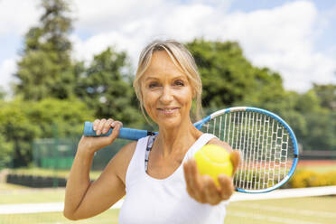 Porträt einer lächelnden reifen Frau, die einen Tennisball im Tennisclub hält - WPEF01765