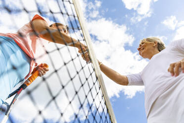 Reife Frauen beenden ein Tennisspiel und schütteln sich am Netz die Hände - WPEF01766