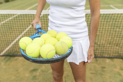 Tennisspielerin hält einen Tennisschläger mit Bällen auf einem Rasenplatz - WPEF01783