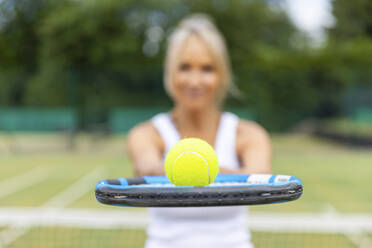 Nahaufnahme einer Frau, die einen Tennisschläger mit einem Ball in einem Tennisclub hält - WPEF01785