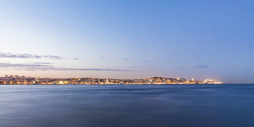 Beleuchtetes Stadtbild am Fluss Tejo gegen den Himmel bei Sonnenuntergang, Lissabon, Portugal - WDF05390