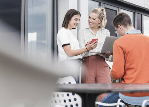 Lässige Geschäftsleute mit Smartphone und Laptop treffen sich auf der Dachterrasse, lizenzfreies Stockfoto