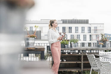 Casual businesswoman with cell phone on roof terrace - UUF18552