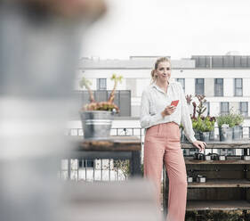 Porträt einer lässigen Geschäftsfrau mit Mobiltelefon auf einer Dachterrasse - UUF18554