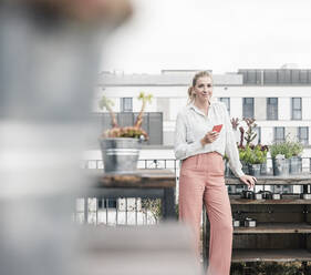 Portrait of casual businesswoman with cell phone on roof terrace - UUF18554