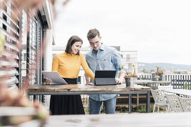 Casual businessman and woman with documents and tablet meeting on roof terrace - UUF18560