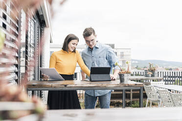 Lässiger Geschäftsmann und Frau mit Dokumenten und Tablet bei einem Treffen auf der Dachterrasse - UUF18560