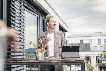 Businesswoman with coffee cup and tablet on roof terrace - UUF18566