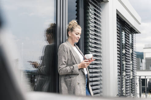 Geschäftsfrau mit Mobiltelefon und Kaffeetasse auf der Dachterrasse - UUF18572